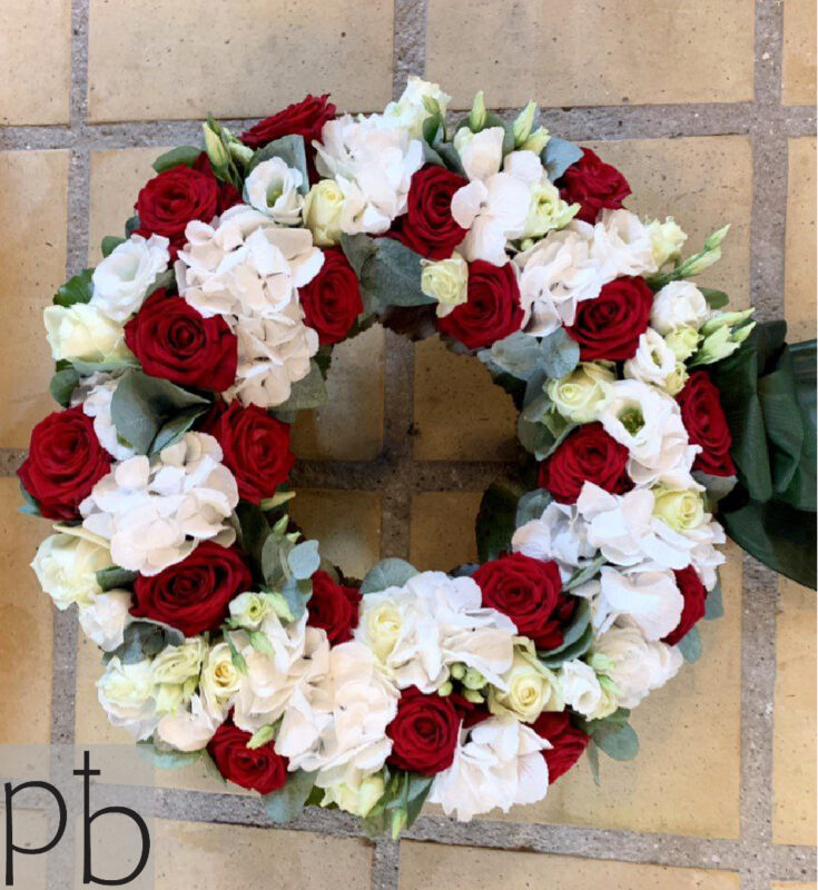 Hjerteformet sorgkrans med hvide liljer, roser og eukalyptus bundet med silkebånd klar til begravelse i Farum (3520)